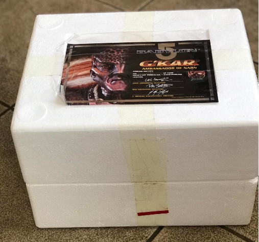 White foam box with a business card featuring a logo and text on a tiled floor.