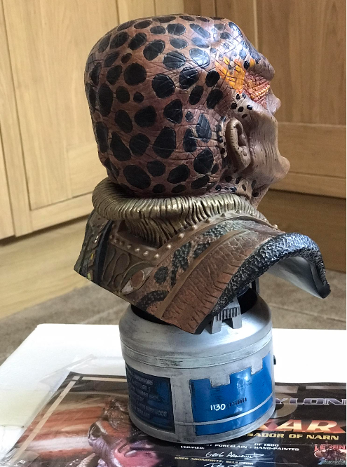 Decorative bust of a character with leopard print head on a cylindrical base, placed on a surface with a magazine underneath.
