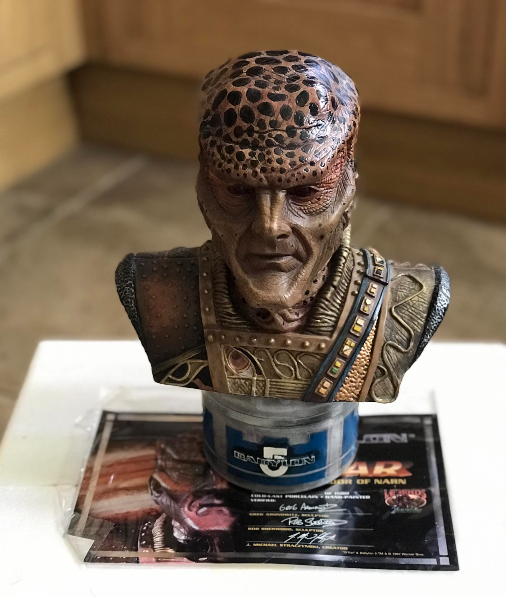 Bronze bust of a character with detailed armor and headpiece on a stand with promotional material.