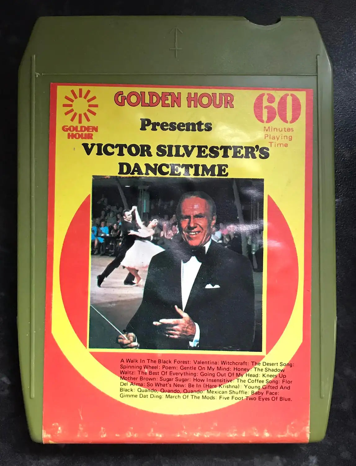 Vintage olive green 8-track cassette, "Golden Hour Presents Victor Silvester's Dancetime," with a man in a tuxedo.